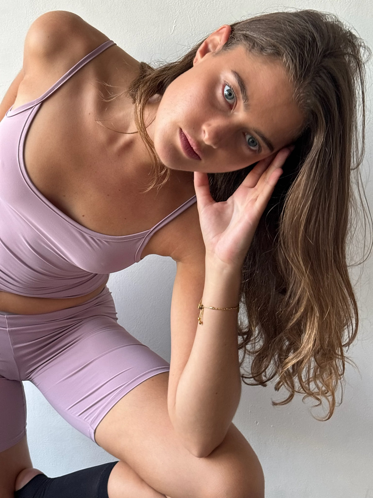A woman wearing a matching lavender sports bra and biker shorts set, posing against a plain light gray wall.